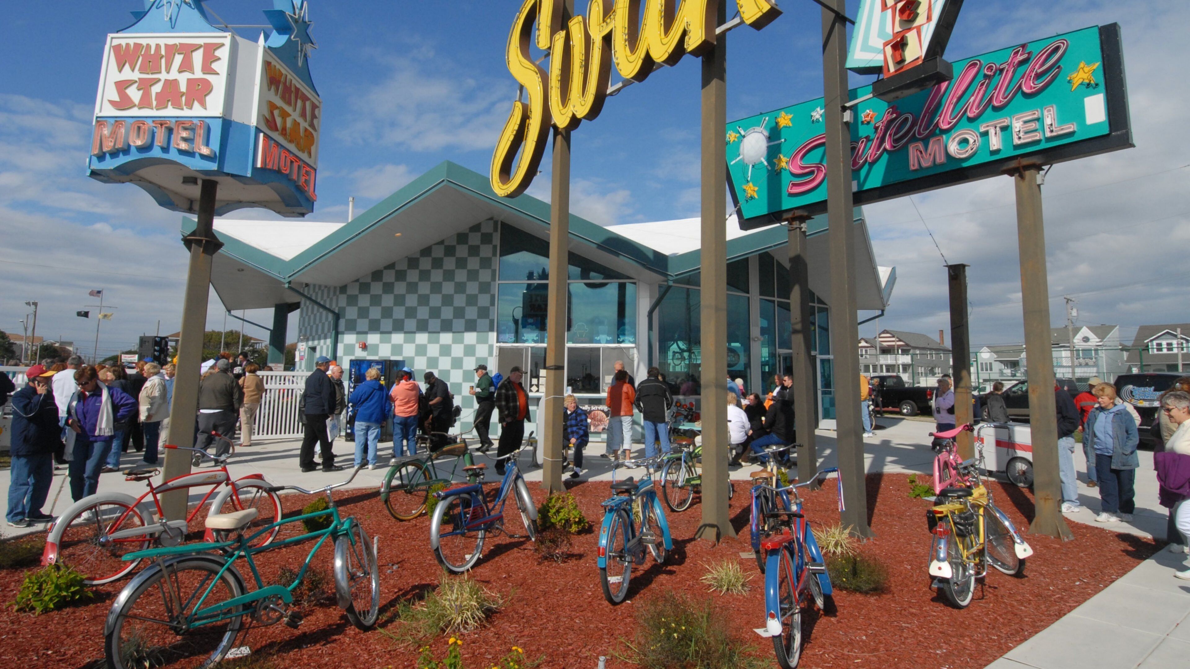 A motel with neon signs, a crowd of people, and bicycles.