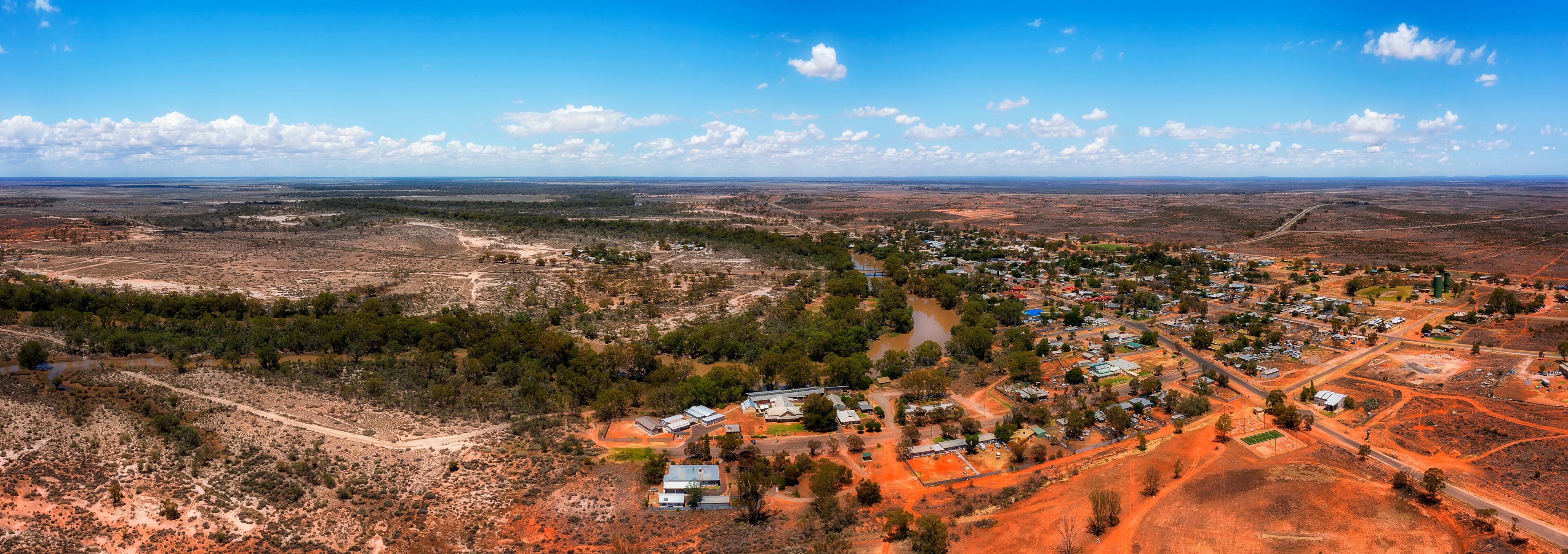A town nestled in a semi-arid landscape with sparse vegetation, surrounded by open fields and a few scattered trees.
