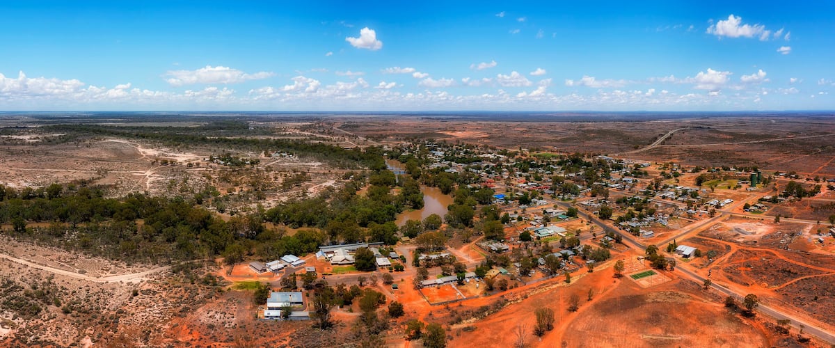 A town nestled in a semi-arid landscape with sparse vegetation, surrounded by open fields and a few scattered trees.