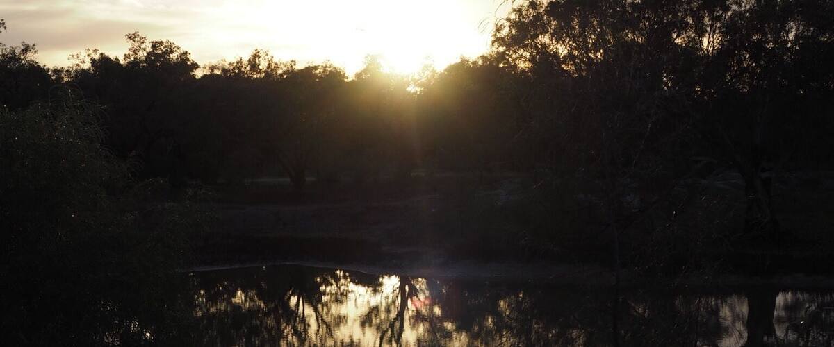 A sunset over a calm lake with trees reflecting the sky.