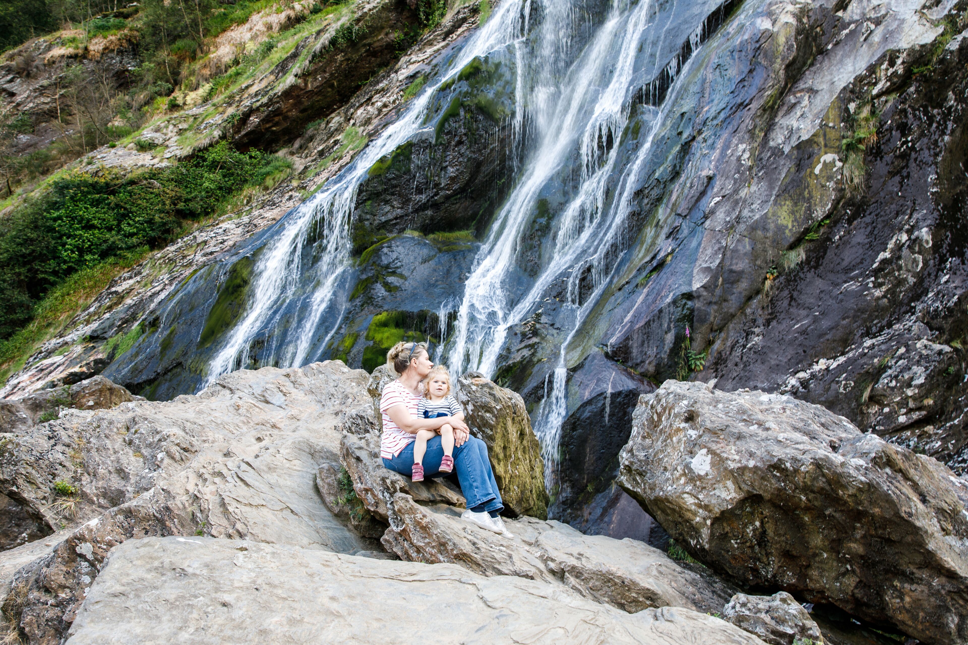 A waterfall cascading over rocks with a person and child sitting on a rock in front.