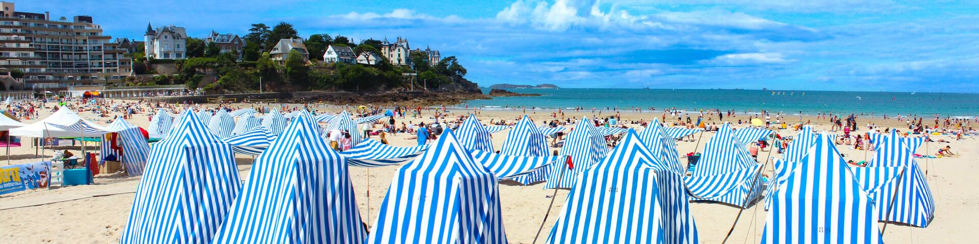 A beach with striped umbrellas and a coastal town in the background.