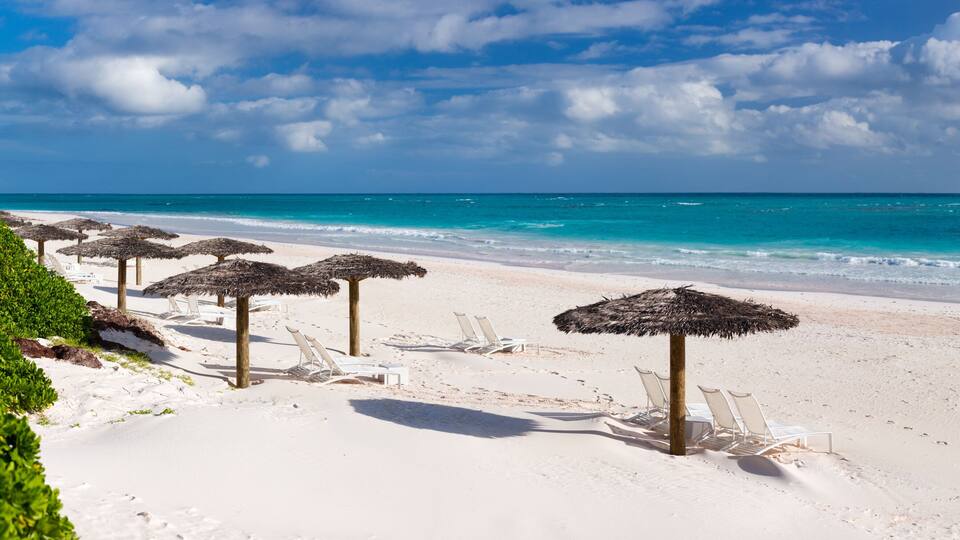 A beach with white sand, turquoise water, and thatched umbrellas.