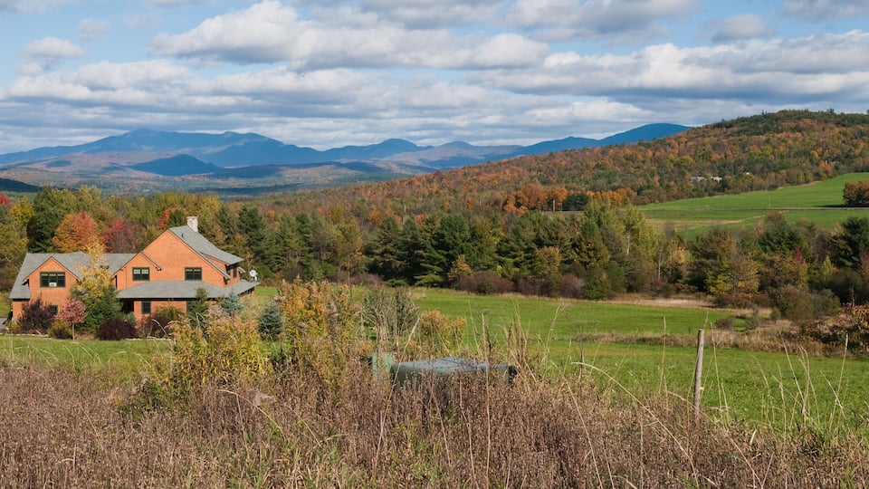 A house surrounded by autumn foliage, a green field, and distant mountains.