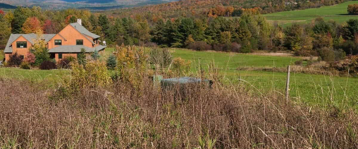A house surrounded by autumn foliage, a green field, and distant mountains.