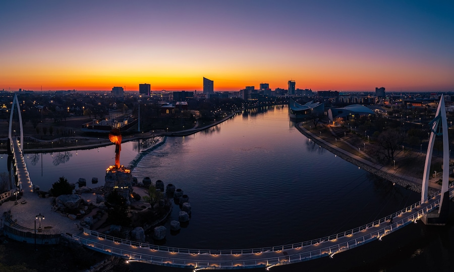 Un coucher de soleil sur une rivière, avec un pont et la silhouette de la ville en arrière-plan.