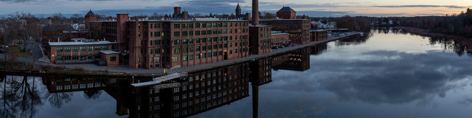 Aerial view of the historic Watch City industrial complex mirrored in the tranquil Charles River under a twilight sky. Waltham, Massachusetts, USA.