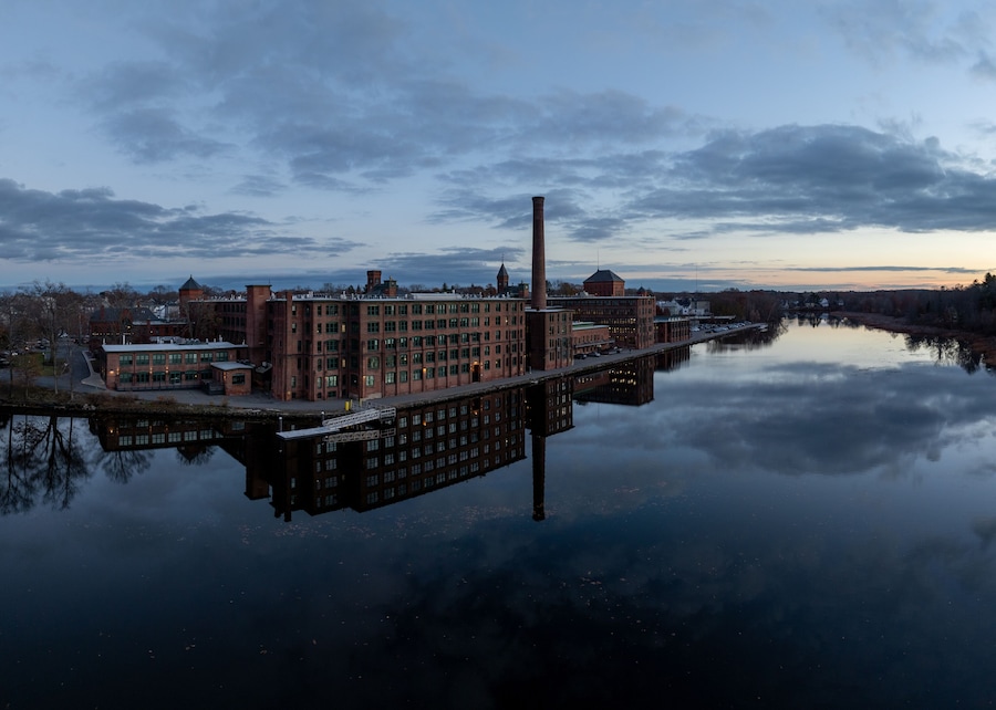 Aerial view of the historic Watch City industrial complex mirrored in the tranquil Charles River under a twilight sky. Waltham, Massachusetts, USA.