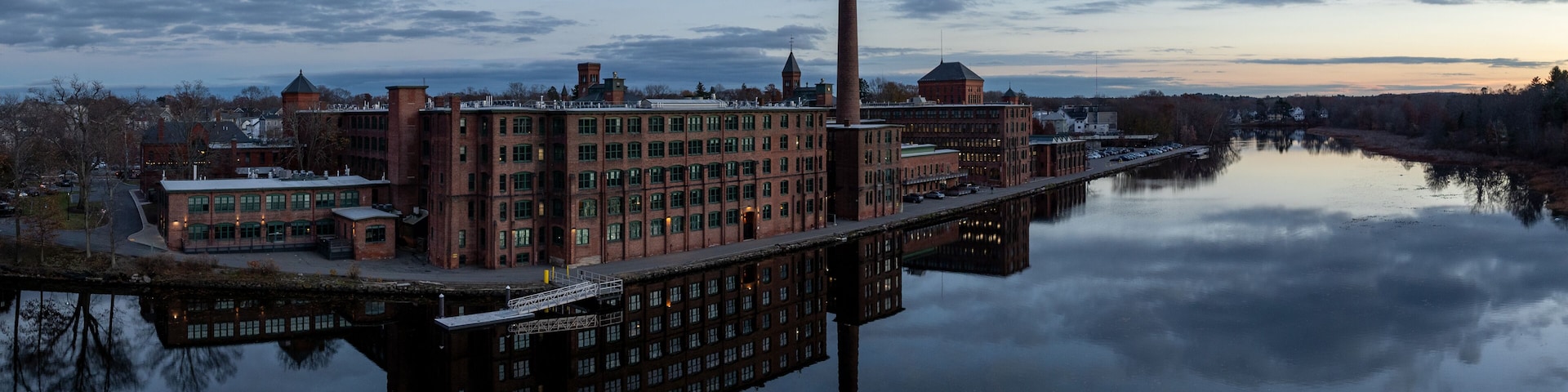 Aerial view of the historic Watch City industrial complex mirrored in the tranquil Charles River under a twilight sky. Waltham, Massachusetts, USA.