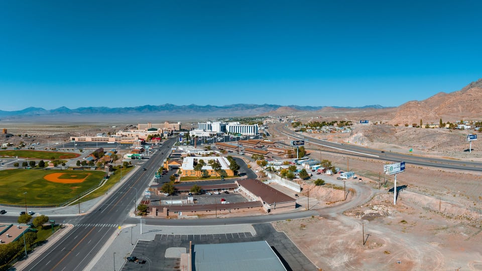 A town with a baseball field, roads, buildings, and mountains in the background.