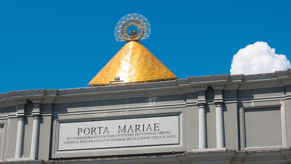 Eine goldene Kuppel mit einem runden Wappen obenauf, und eine darunterliegende Schilder mit der Aufschrift 'PORTA MARIAE'.