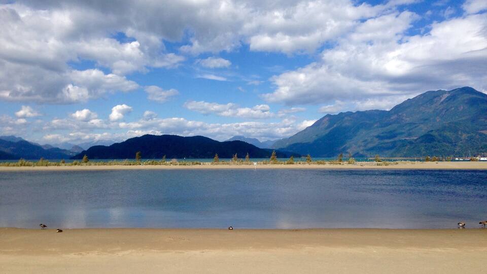 A beach with mountains in the background and a partly cloudy sky.