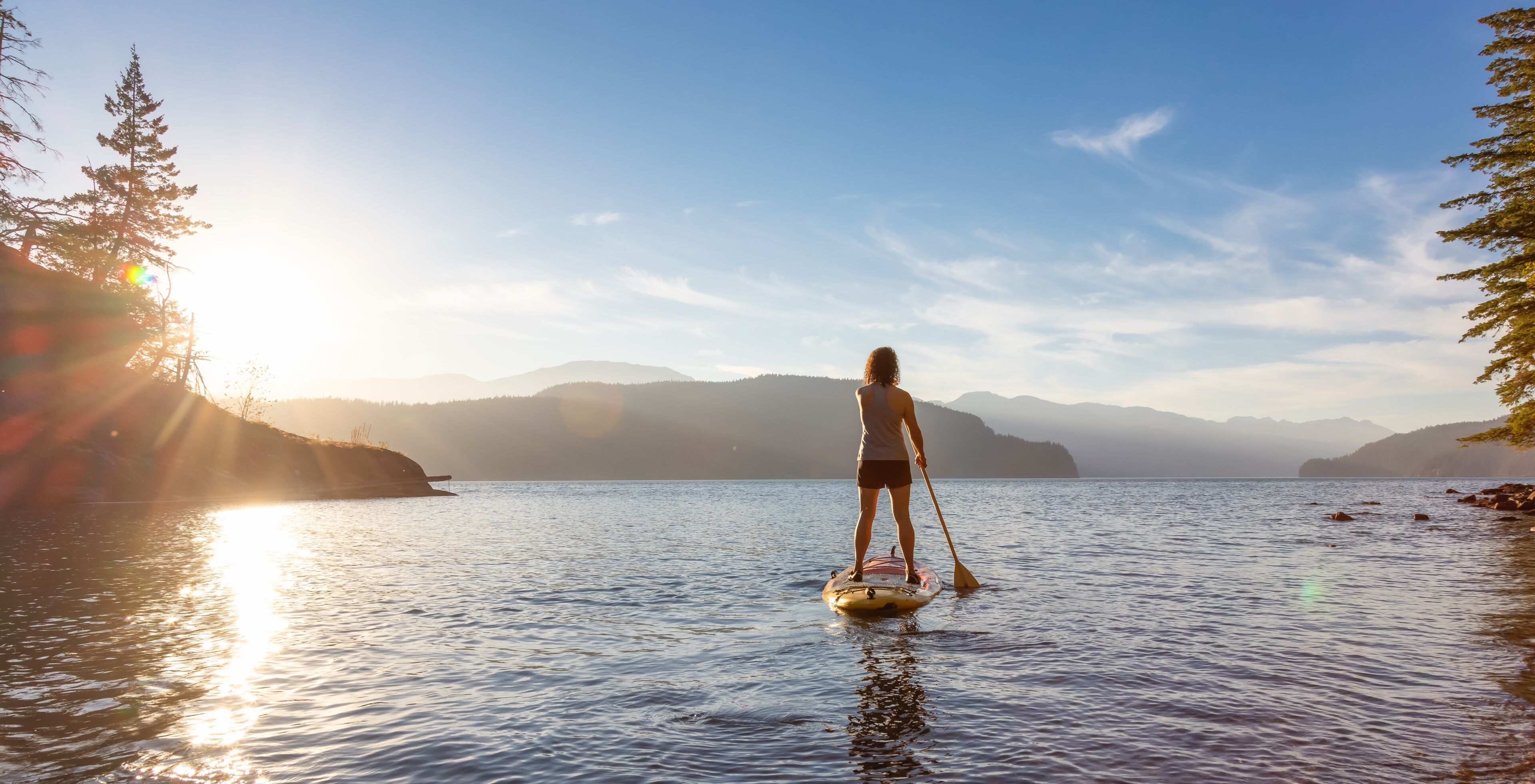Adventurous Woman Paddling on a Paddle Board in a peaceful lake.
