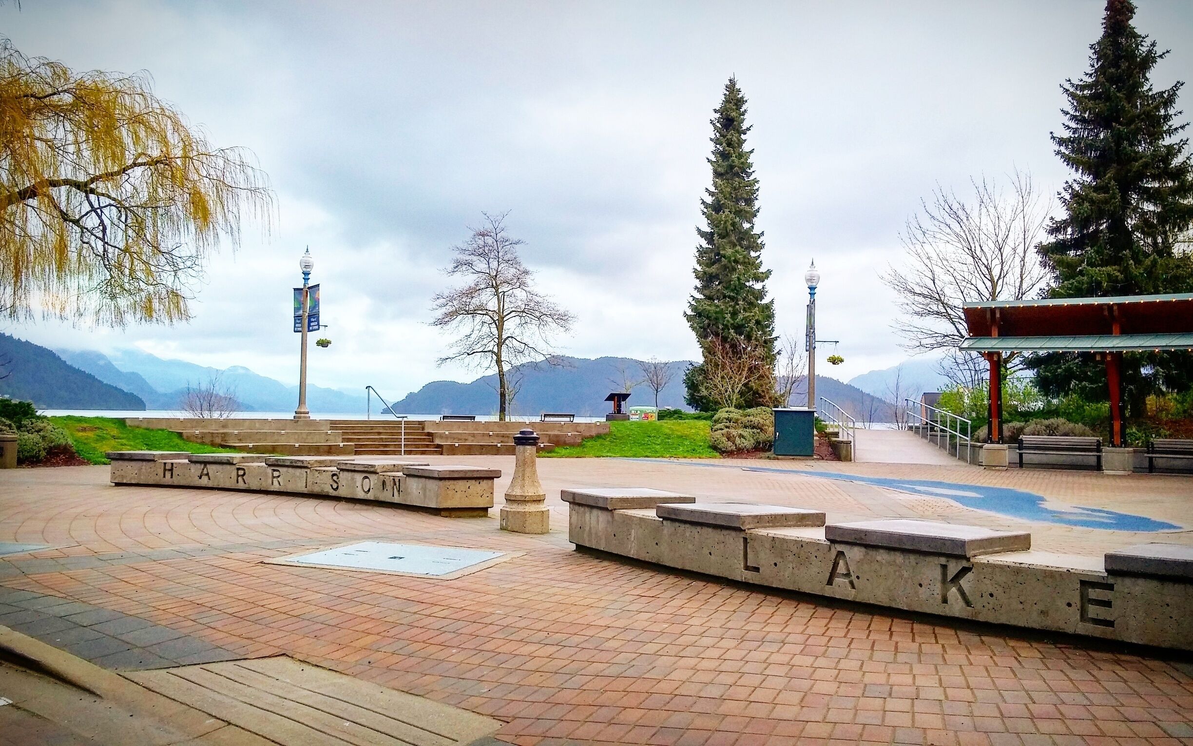 A park with a concrete pathway, benches, and a sign that reads "HARRISON LAKE".