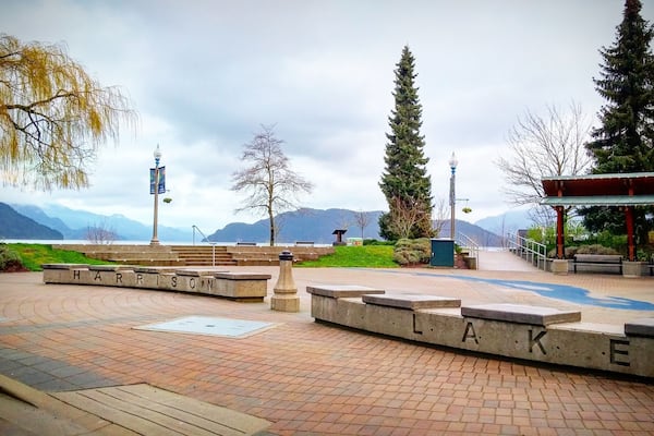 A park with a concrete pathway, benches, and a sign that reads "HARRISON LAKE".
