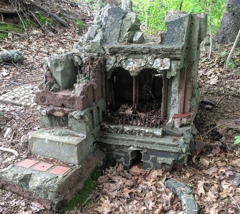 A weathered stone structure with steps and a small opening, surrounded by fallen leaves and moss.