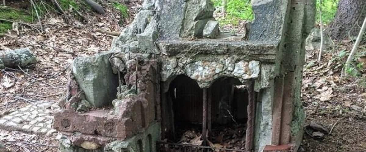 A weathered stone structure with steps and a small opening, surrounded by fallen leaves and moss.