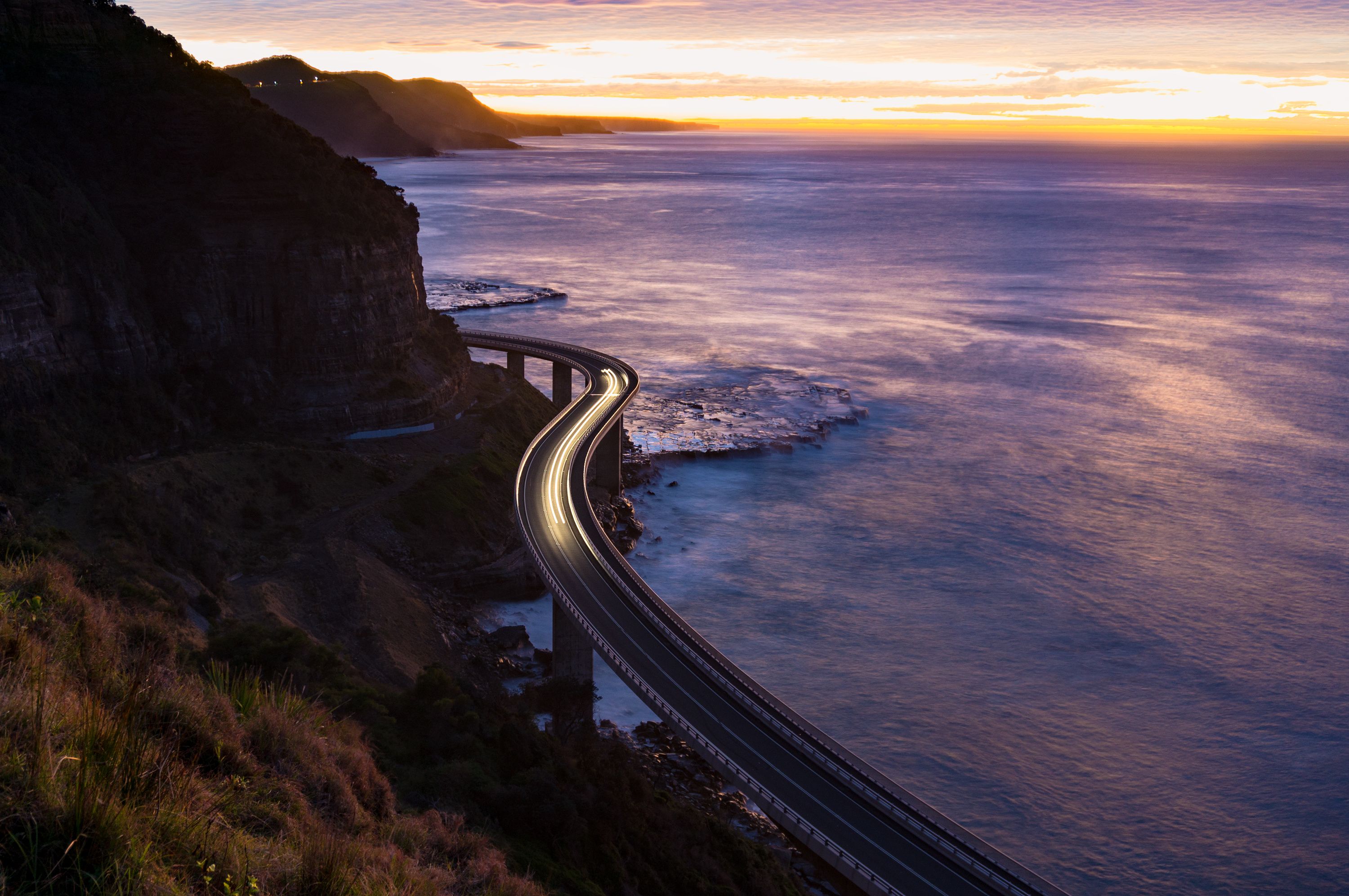 A coastal road curving along a cliffside with the ocean in the background.