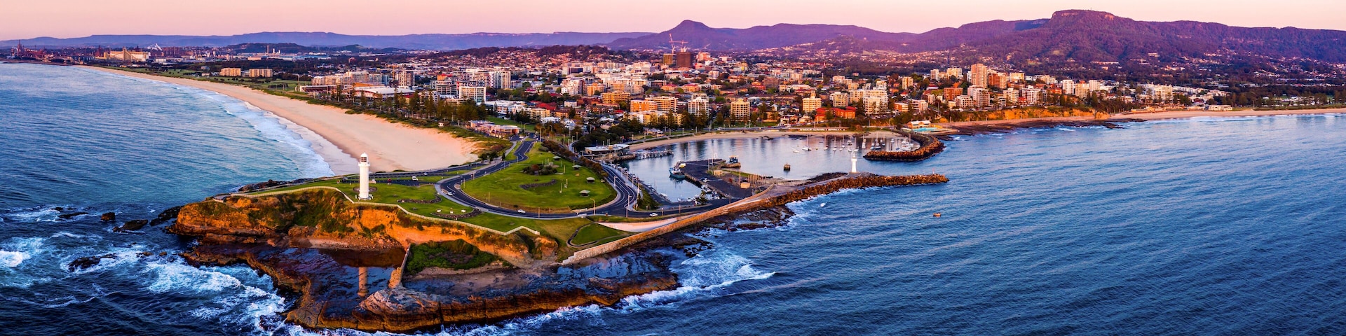 Une vue aérienne d’une ville côtière, avec un phare imposant, une plage et un paysage montagneux en arrière-plan.