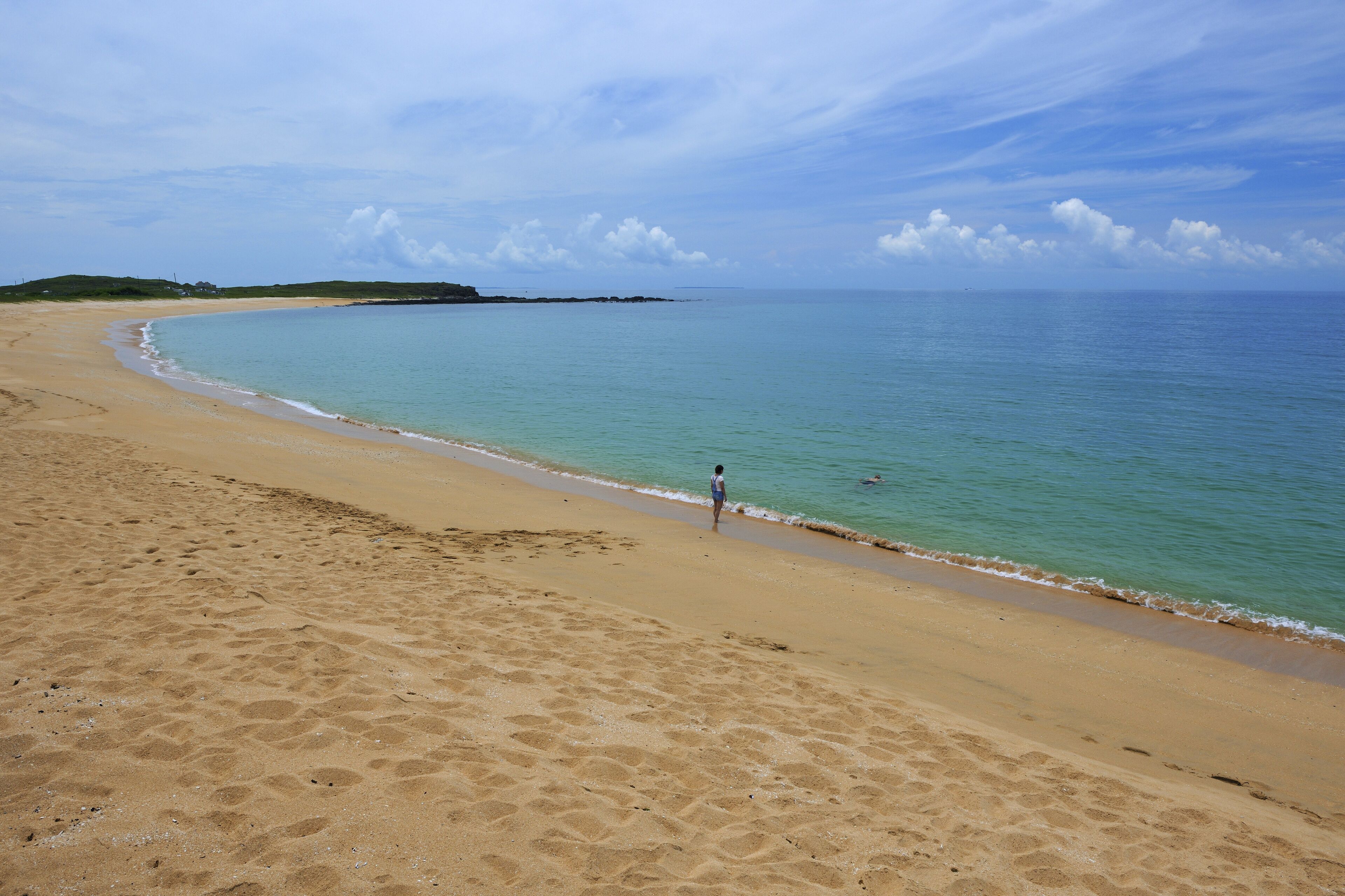 A sandy beach with gentle waves, a clear sky, and a distant shoreline.