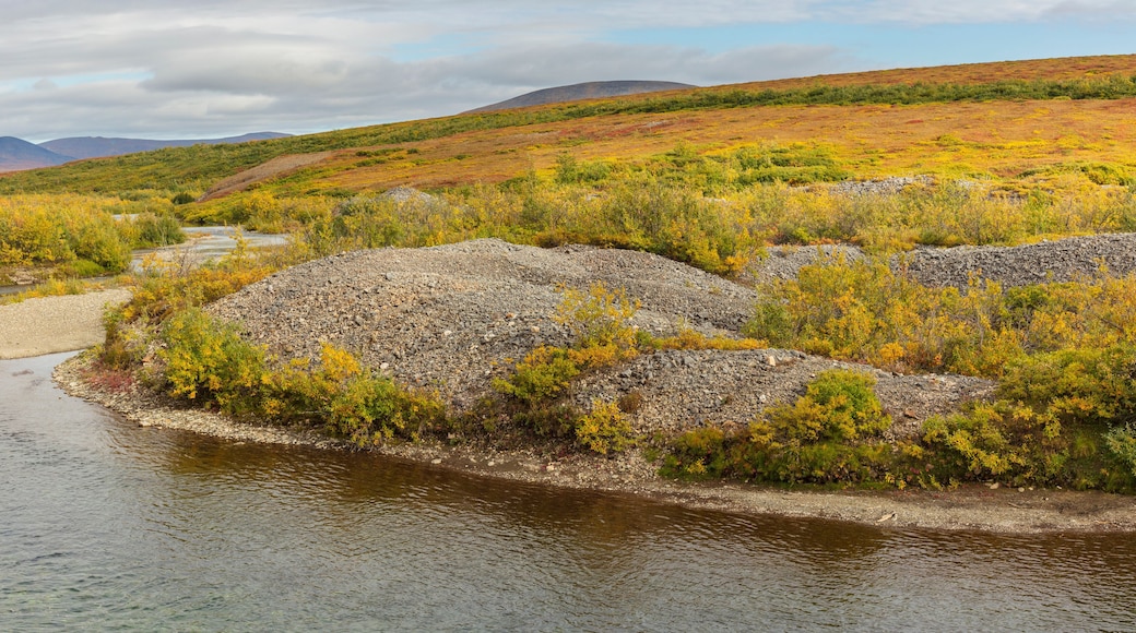 Tundra landscape in Western Alaska with rolling hills piles of mine tailings left behind by a gold dredge and river in autumn colors in the vicinity of Nome, Alaska