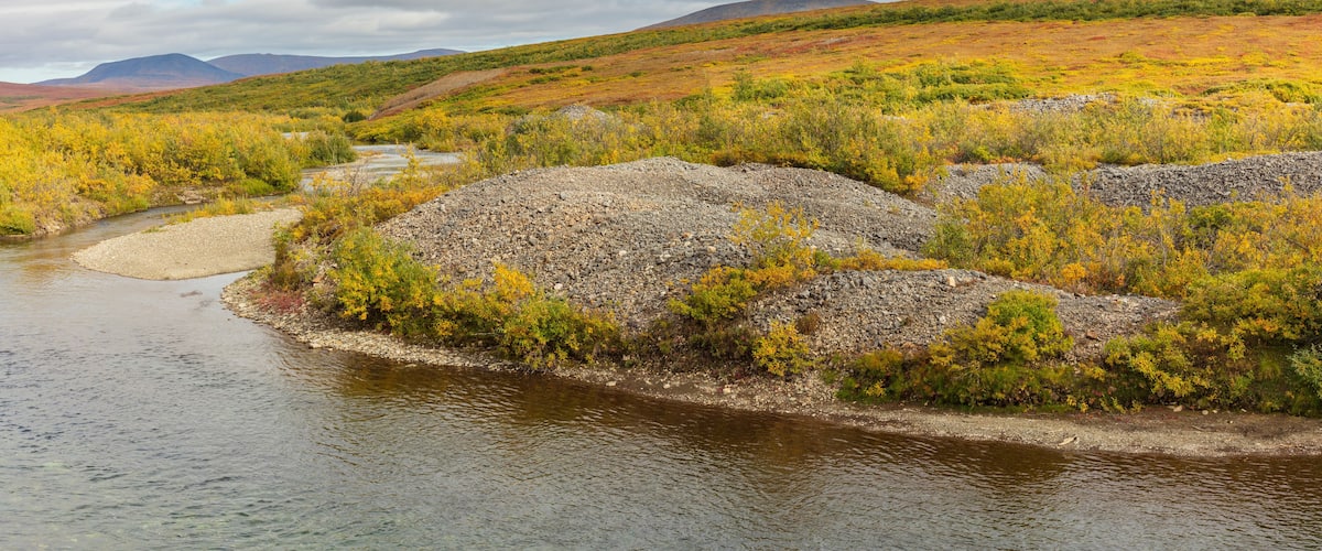 A river winding through a hilly landscape with autumn-colored vegetation and distant mountains.