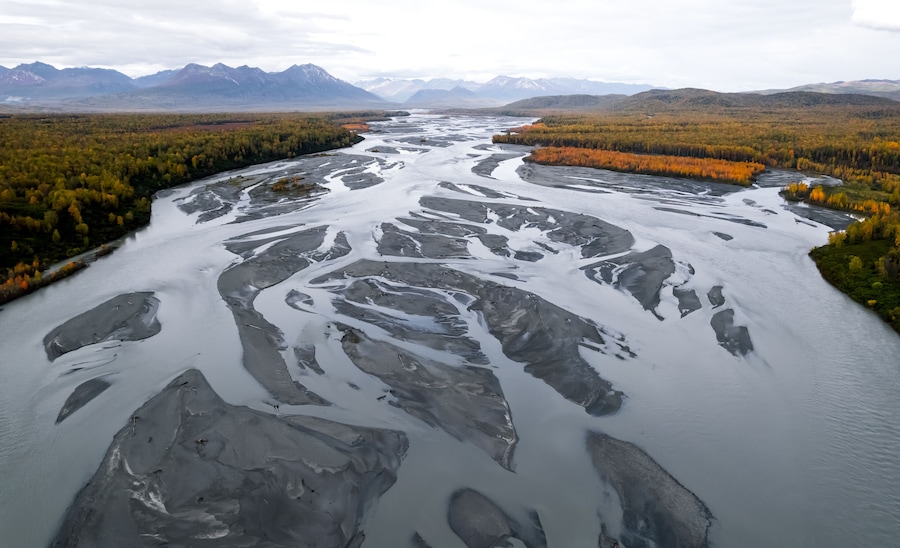 Un río con formaciones de hielo, rodeado de árboles de colores otoñales y montañas al fondo.