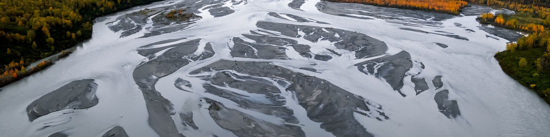 Un río con formaciones de hielo, rodeado de árboles de colores otoñales y montañas al fondo.