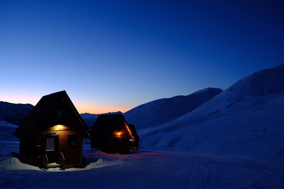 Dos cabañas de madera en un paisaje nevado al anochecer.