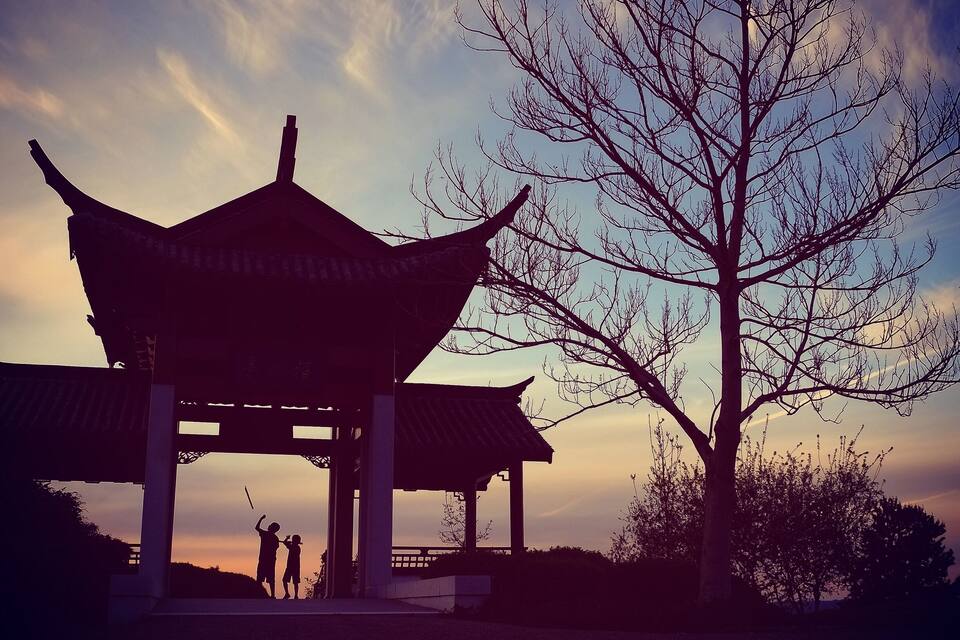 A traditional pavilion with a curved roof silhouette against a sunset sky.