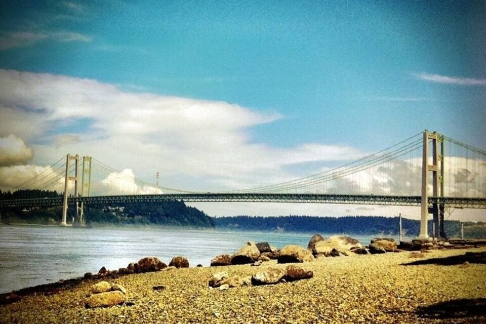 A suspension bridge over a body of water with a rocky shoreline in the foreground.