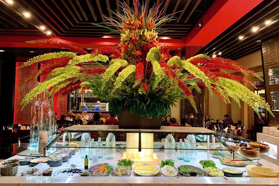 A buffet with various food items and a large floral centerpiece.