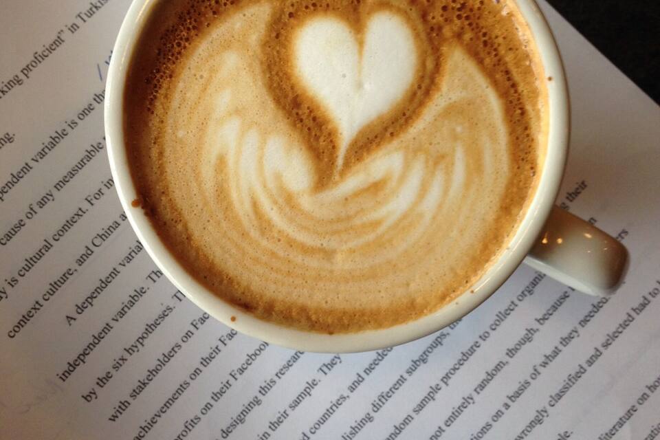 A cup of coffee with a heart-shaped latte art on top, placed on a book.