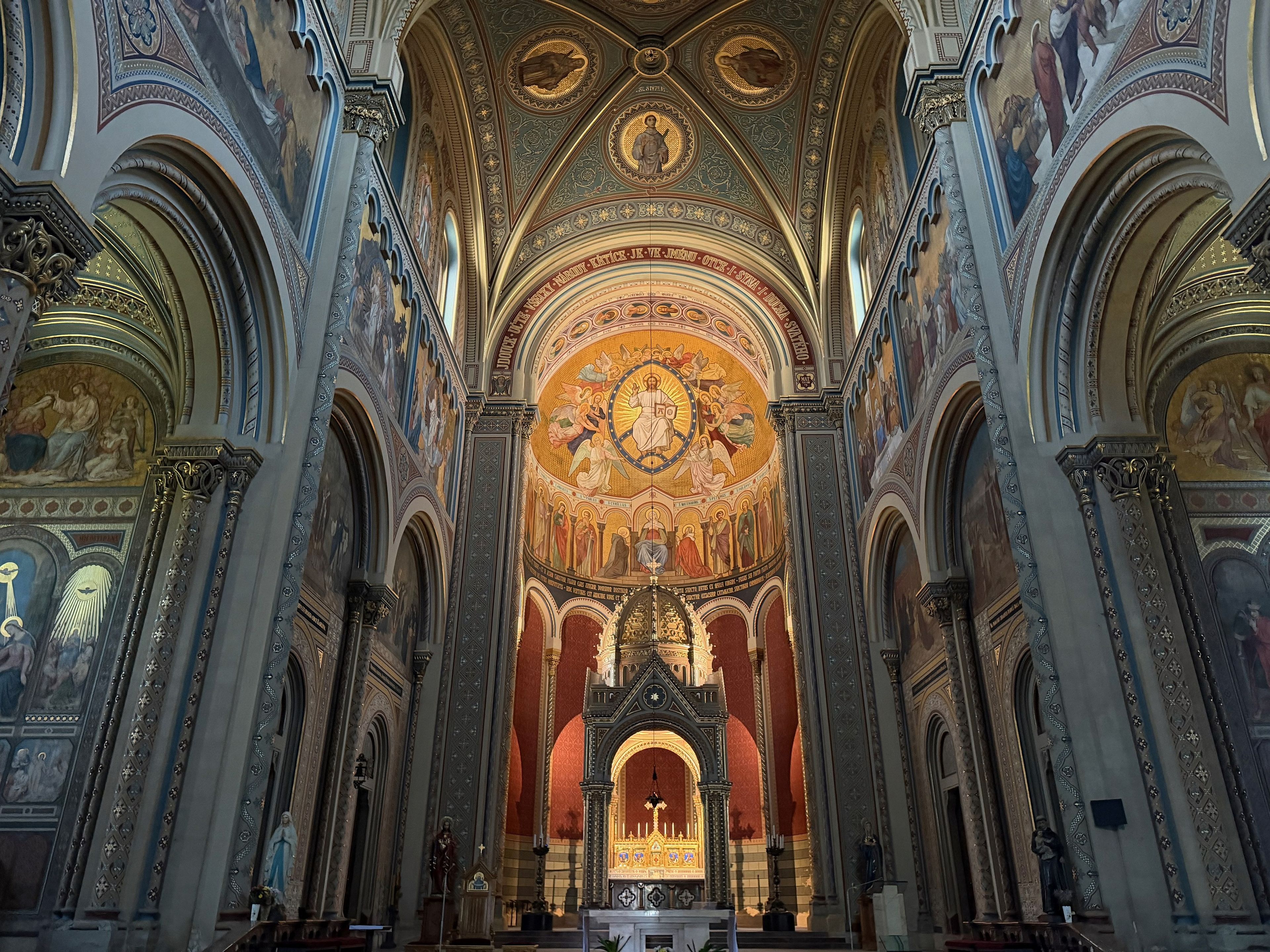 Interior de iglesia ornamentado con frescos detallados, un altar central y un alto techo abovedado.