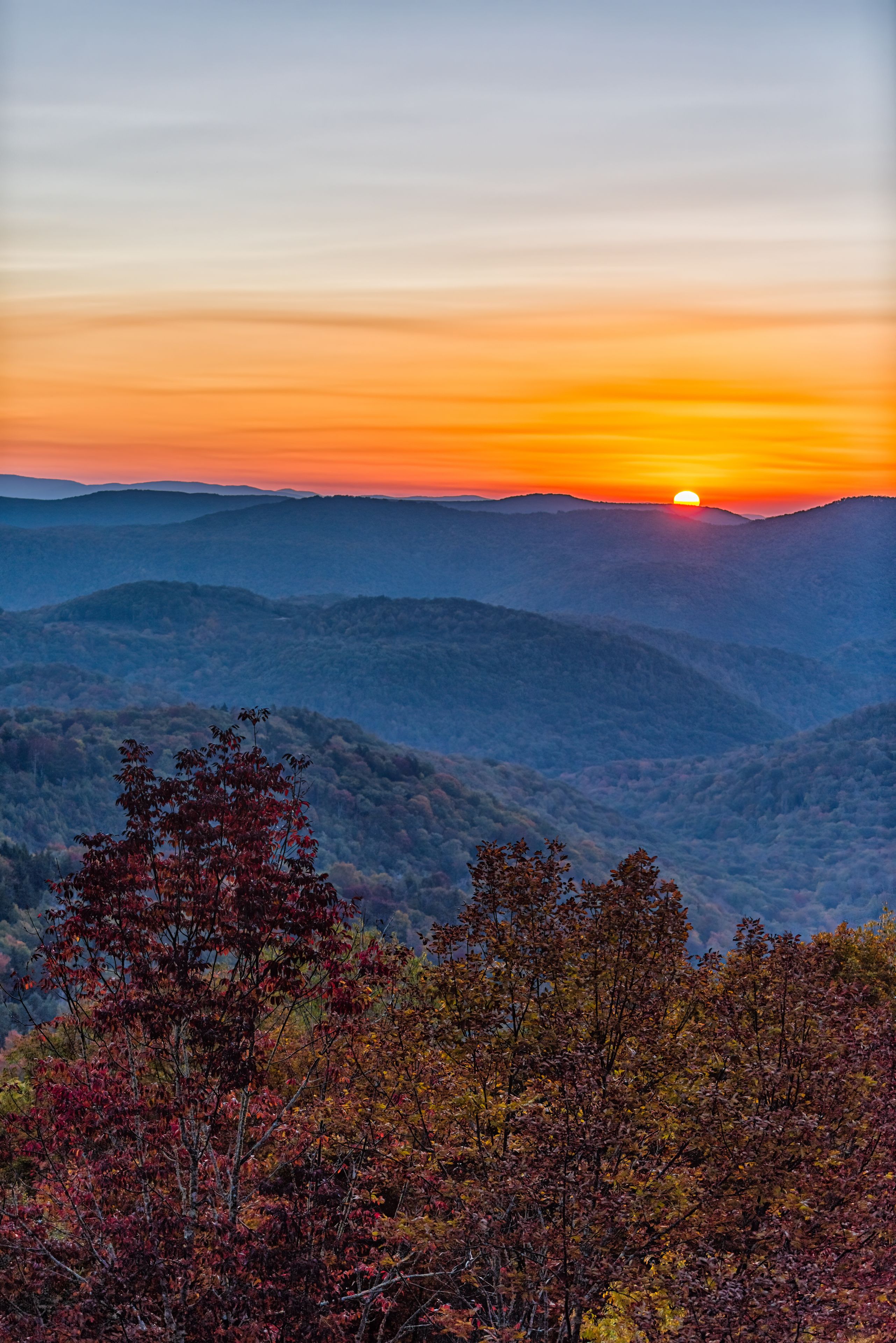 Un atardecer sobre un paisaje montañoso con árboles de colores otoñales en primer plano.