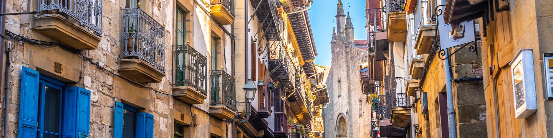 A cobblestone street flanked by historic buildings with ornate balconies and blue shutters.