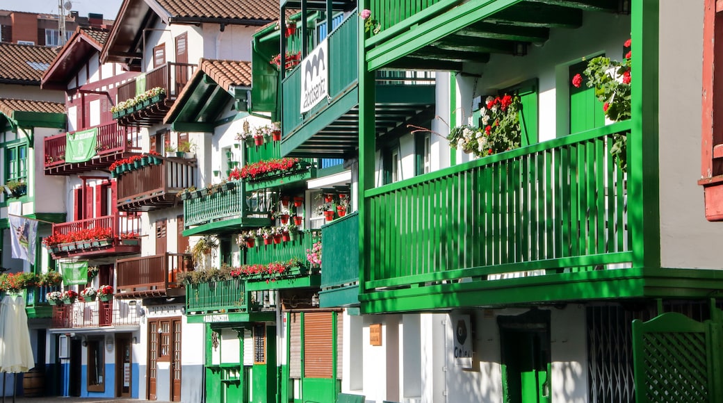 Una calle con edificios de colores, balcones adornados con flores y un letrero con texto.