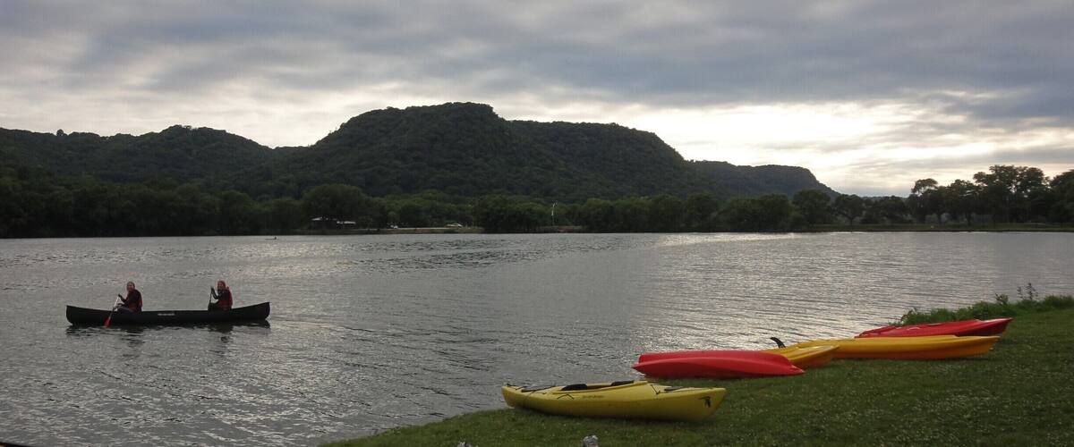 A calm lake with a row of canoes on the shore and a single canoe on the water.