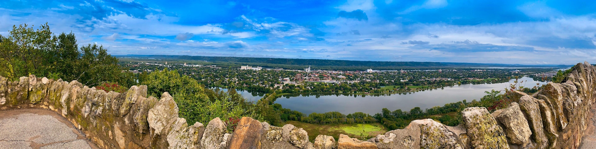 A stone wall with a hole, overlooking a river and a town.