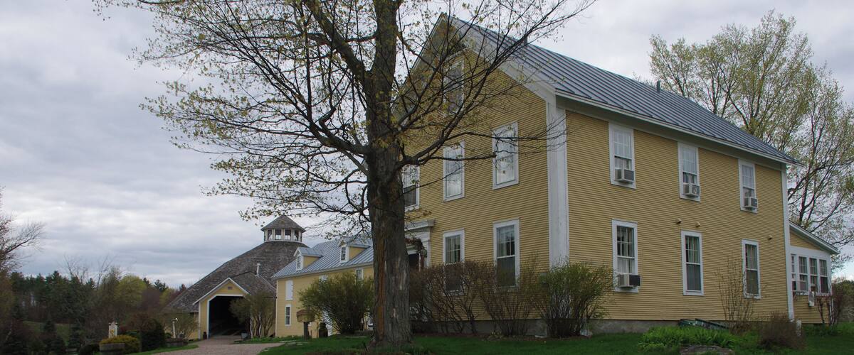 A yellow house with a stone tower, surrounded by a gravel driveway and green grass.