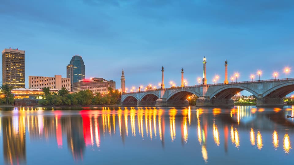 A city skyline with illuminated buildings, a bridge, and a calm river reflecting the lights.