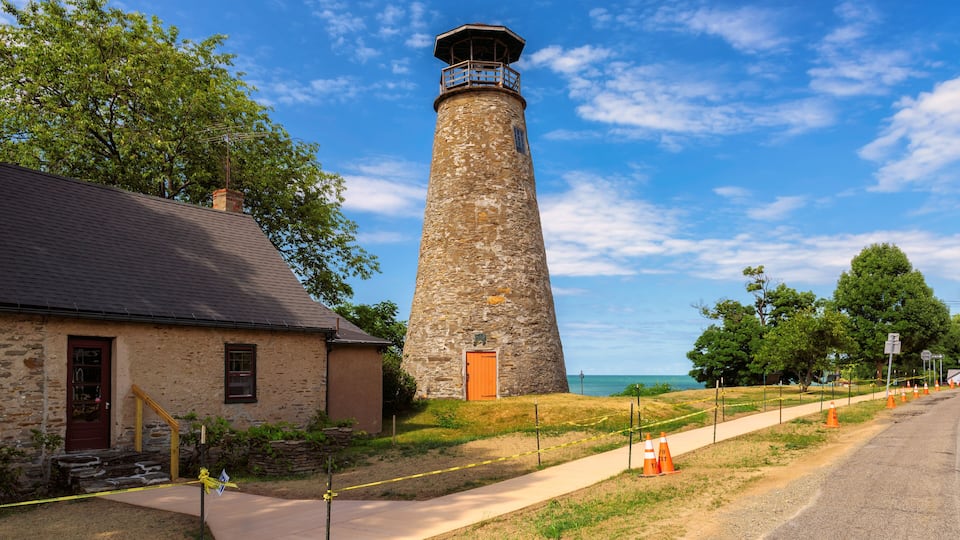 A stone lighthouse with a wooden door, a stone building with a red door, and a clear blue sky.