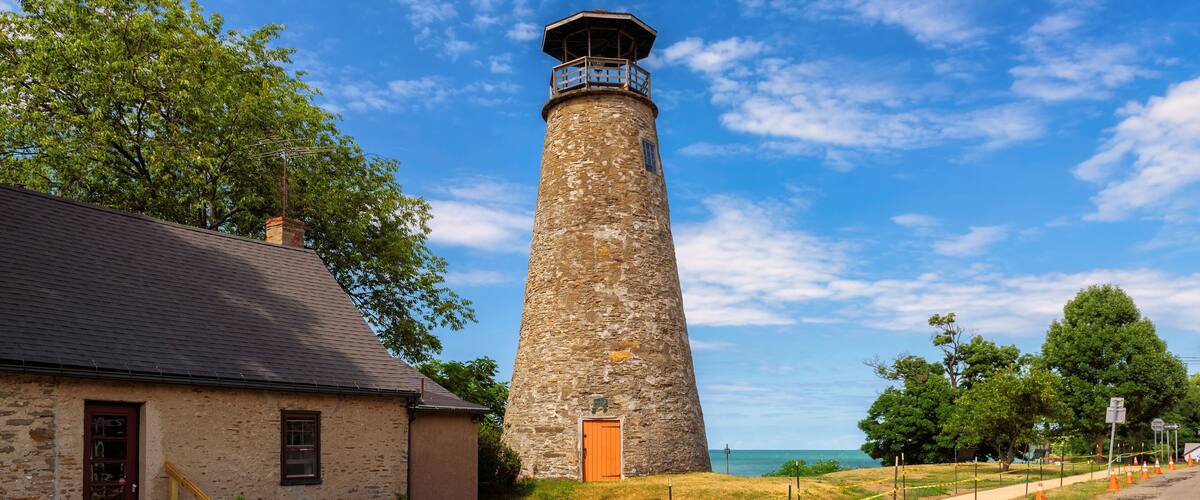 A stone lighthouse with a wooden door, a stone building with a red door, and a clear blue sky.