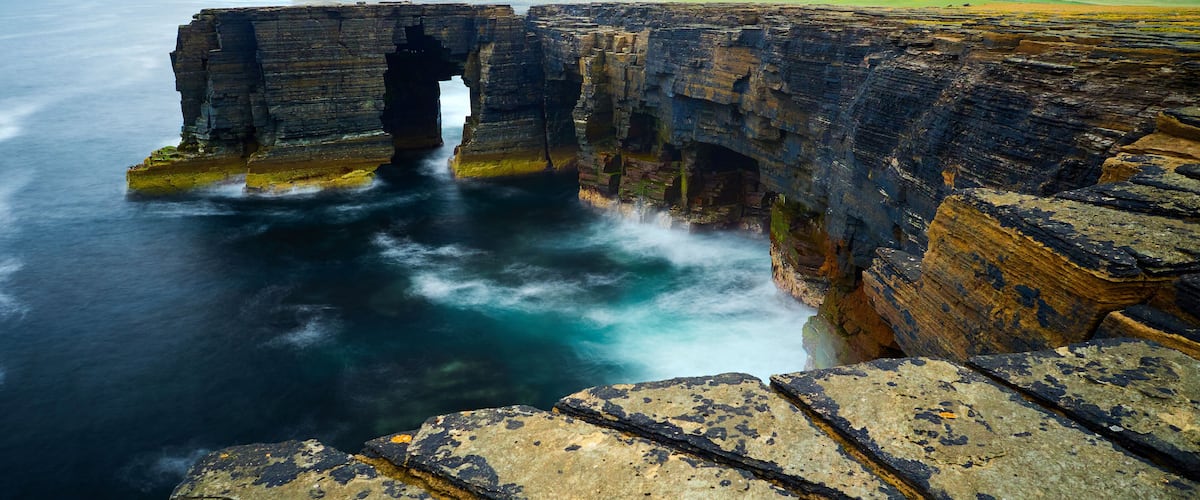 A coastal cliff with a natural arch formation and a narrow passage through it.