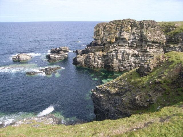 A coastal cliff with layered rock formations and clear blue waters.