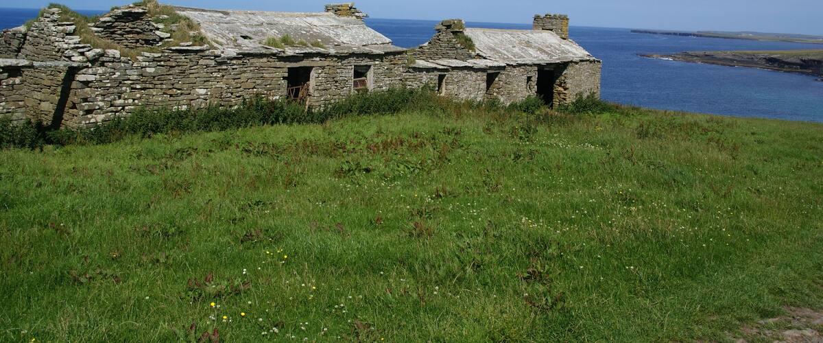 A stone ruin with a grassy foreground and a view of the sea.
