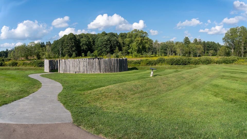 A well-maintained golf course with a winding path, a wooden fence, and a flag on a flagpole.