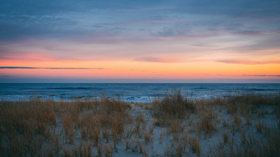 A beach with sand dunes and a sunset over the ocean.