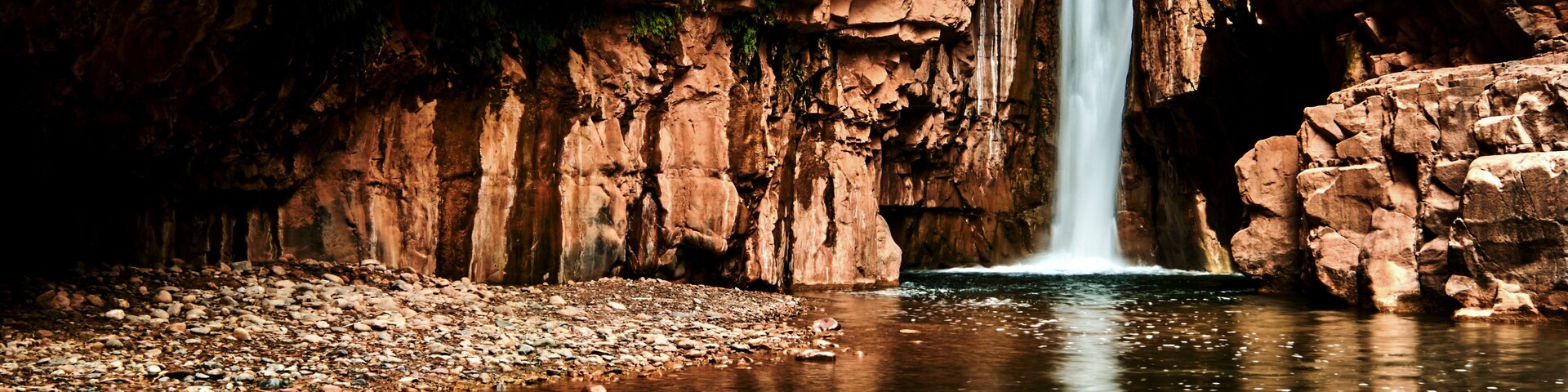 A waterfall cascading into a river surrounded by rocky cliffs.