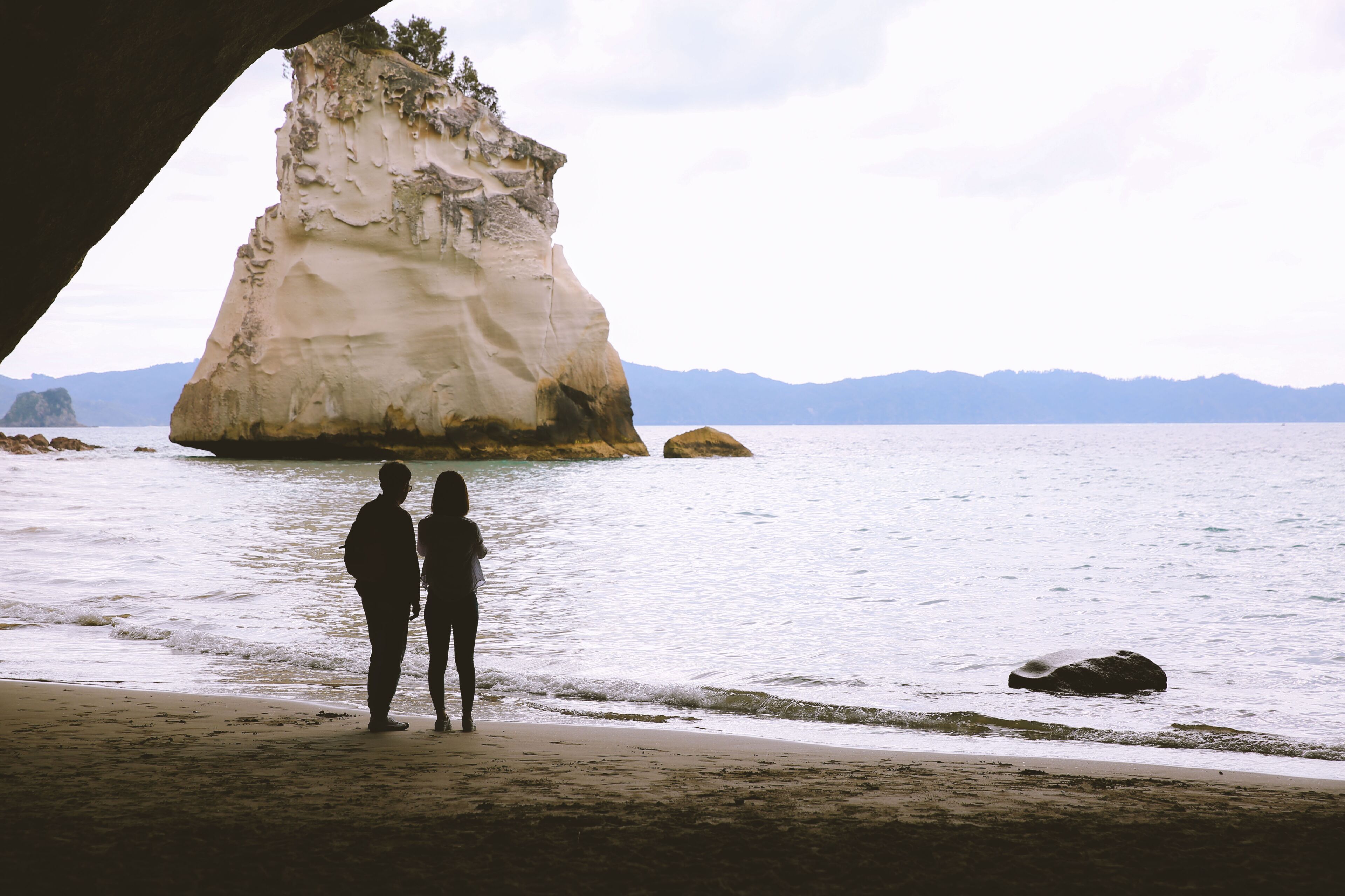 A couple standing on a beach with a large rock formation in the background.